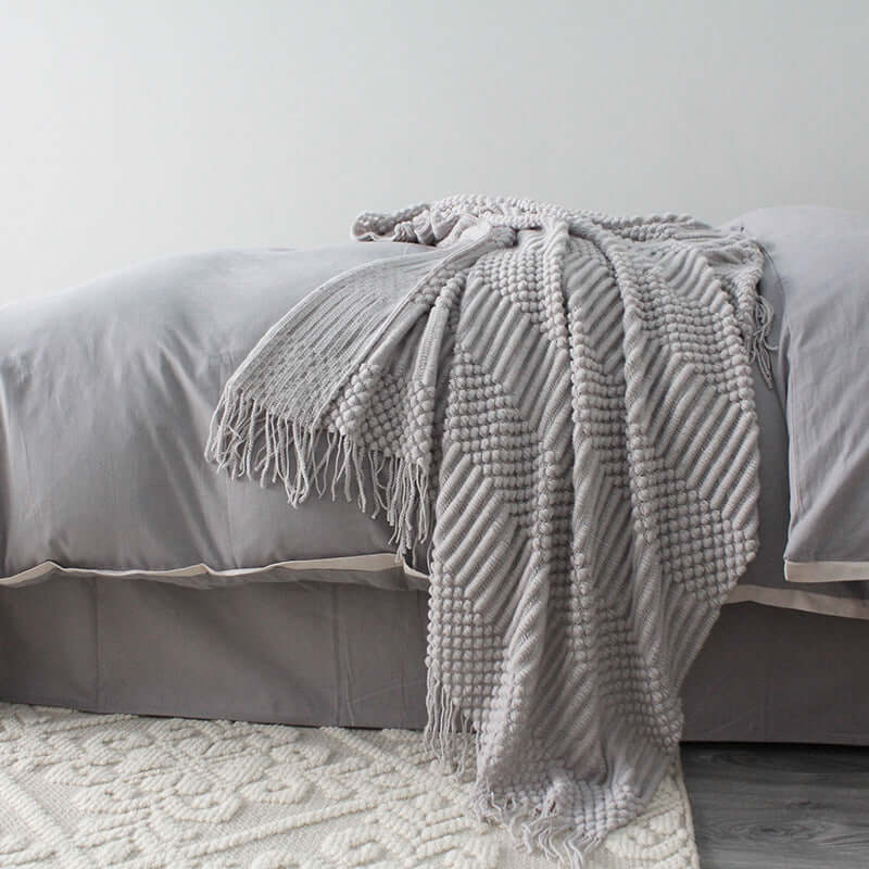 Small grey polyester blanket draped over a bed with textured design, creating a cozy nap environment