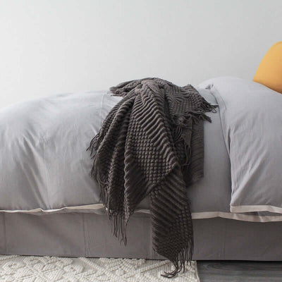 Small gray polyester nap blanket casually draped over a neatly made bed in a serene bedroom setting.