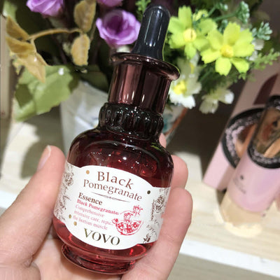 Hand holding a bottle of Black Pomegranate Essence by YOVO with floral background in a cosmetic store.