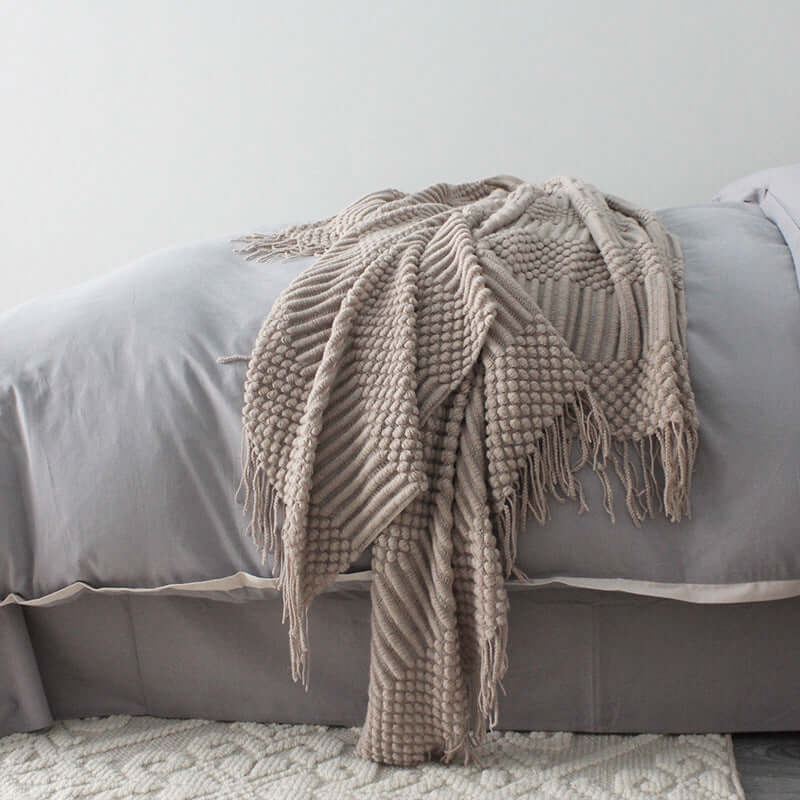 Small textured polyester fiber blanket in taupe draped elegantly over a gray bed, adding a cozy touch to bedroom decor.