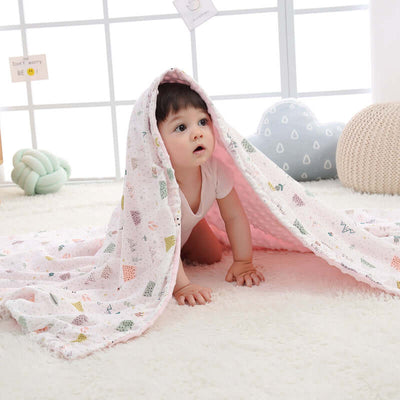 Baby under a pink Doudou blanket with 3D bubble design on a plush white carpet, promoting security and sensory development.