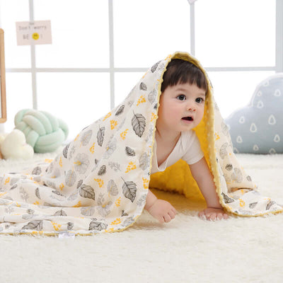 Baby in yellow Doudou blanket with leaf patterns in a cozy room setting, enhancing sensory development.