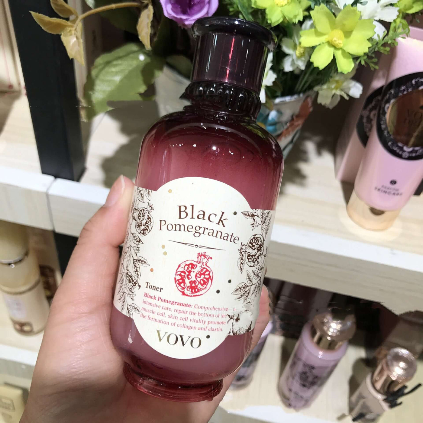 Hand holding a bottle of Vovo Black Pomegranate Toner in front of a cosmetic store shelf.