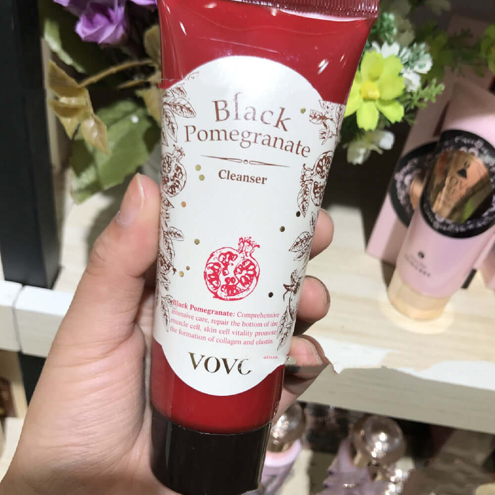 Hand holding a tube of VOV Black Pomegranate Cleanser in a store with floral decor background