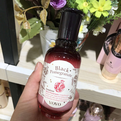 Hand holding a bottle of Black Pomegranate skincare moisturizer in a store, with floral arrangements in the background.